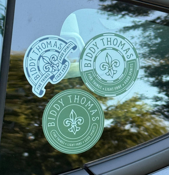 Green stickers with 'Biddy Thomas' branding on a glass surface