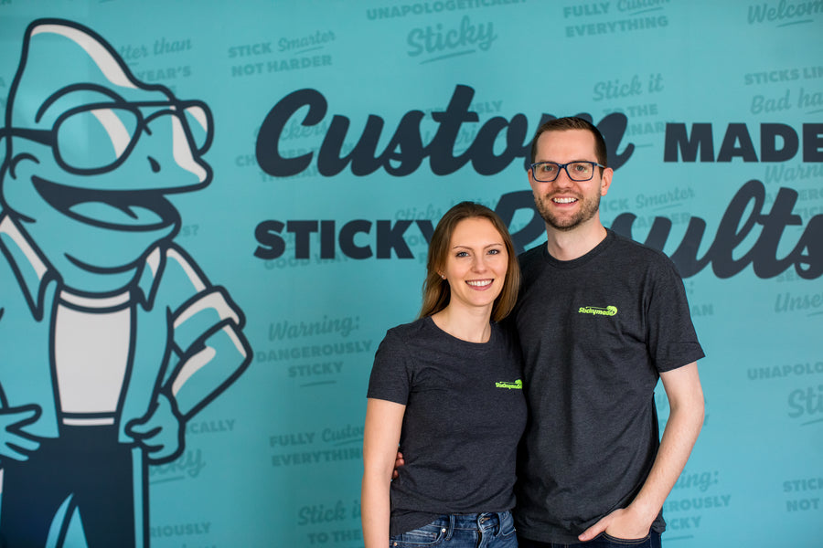Tyler and Alena, Stickymade's founders, in Stickymade shirts in front of a wall with Huey on it